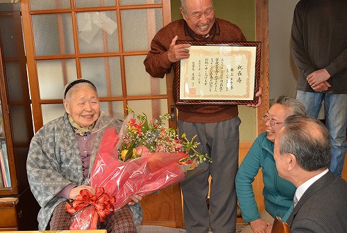 井上タカさんが花束を持ち、男性が賞状を持ち、笑い合っている様子