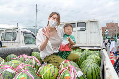 トラクターに積まれたスイカに囲まれた中に女性と幼児が笑顔で写真に写る。