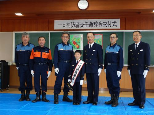 一日消防署長辞令式の様子。中央に笹村さんがおり微笑んだ消防隊員の皆さんとの写真