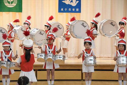 一人の園児が前で指揮を取り、他の園児たちが太鼓を叩いている様子