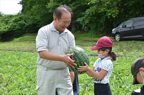 子どもが井上幸彦さんにスイカを渡している様子