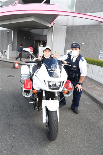 白バイに乗ってピースサインをする男子と警察官